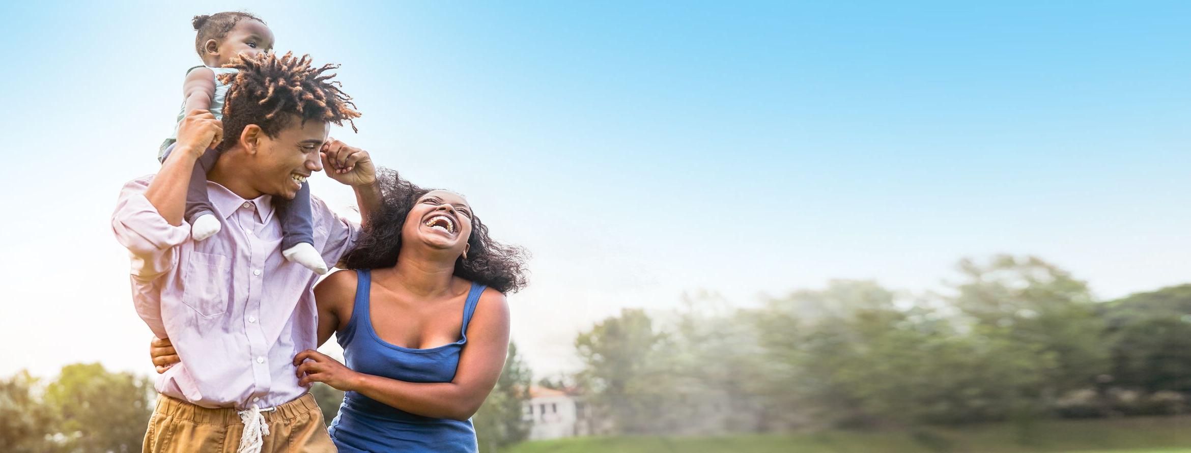 A happy and laughing family outside enjoying each other's company with the daughter on the fathers shoulders